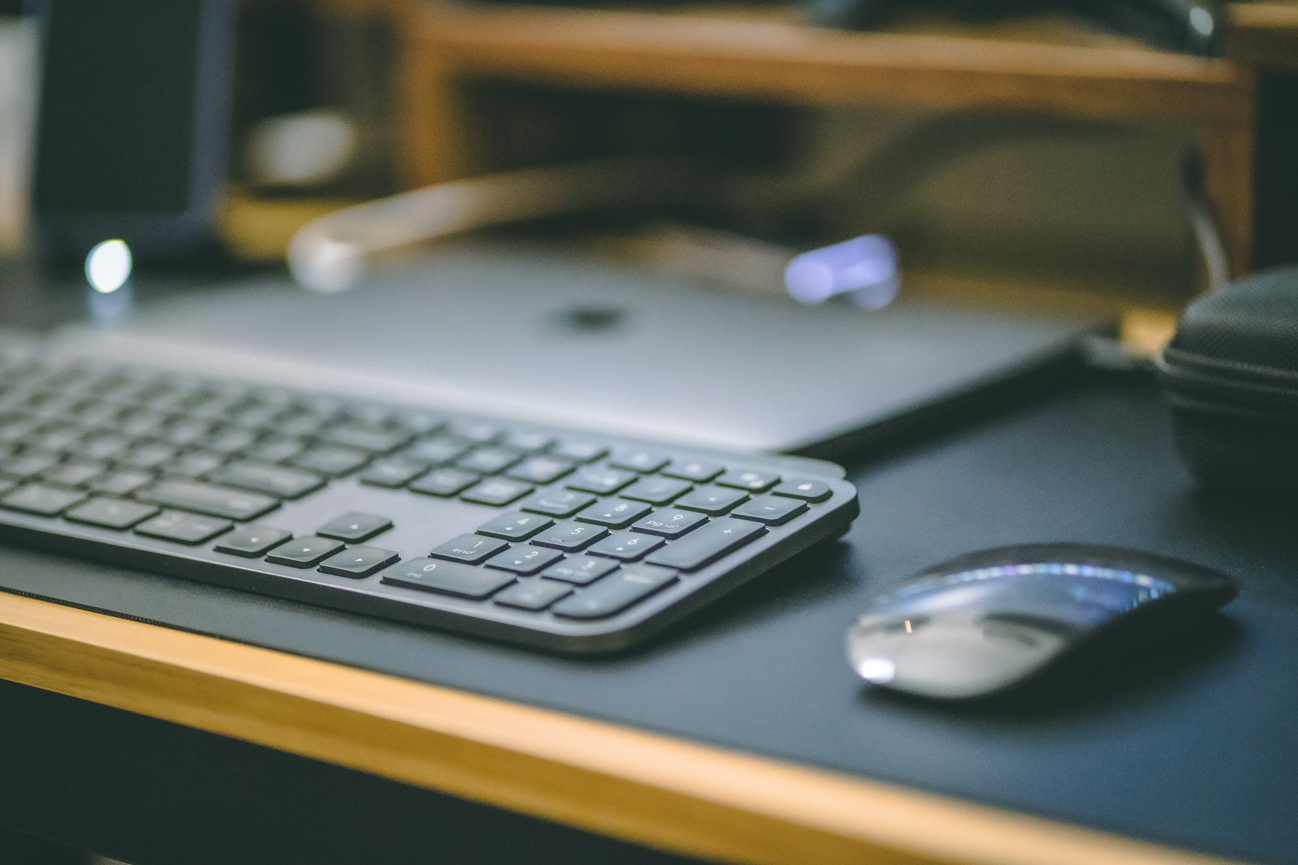 Black trackball mouse with a blue trackball sitting on a wooden desk near a keyboard